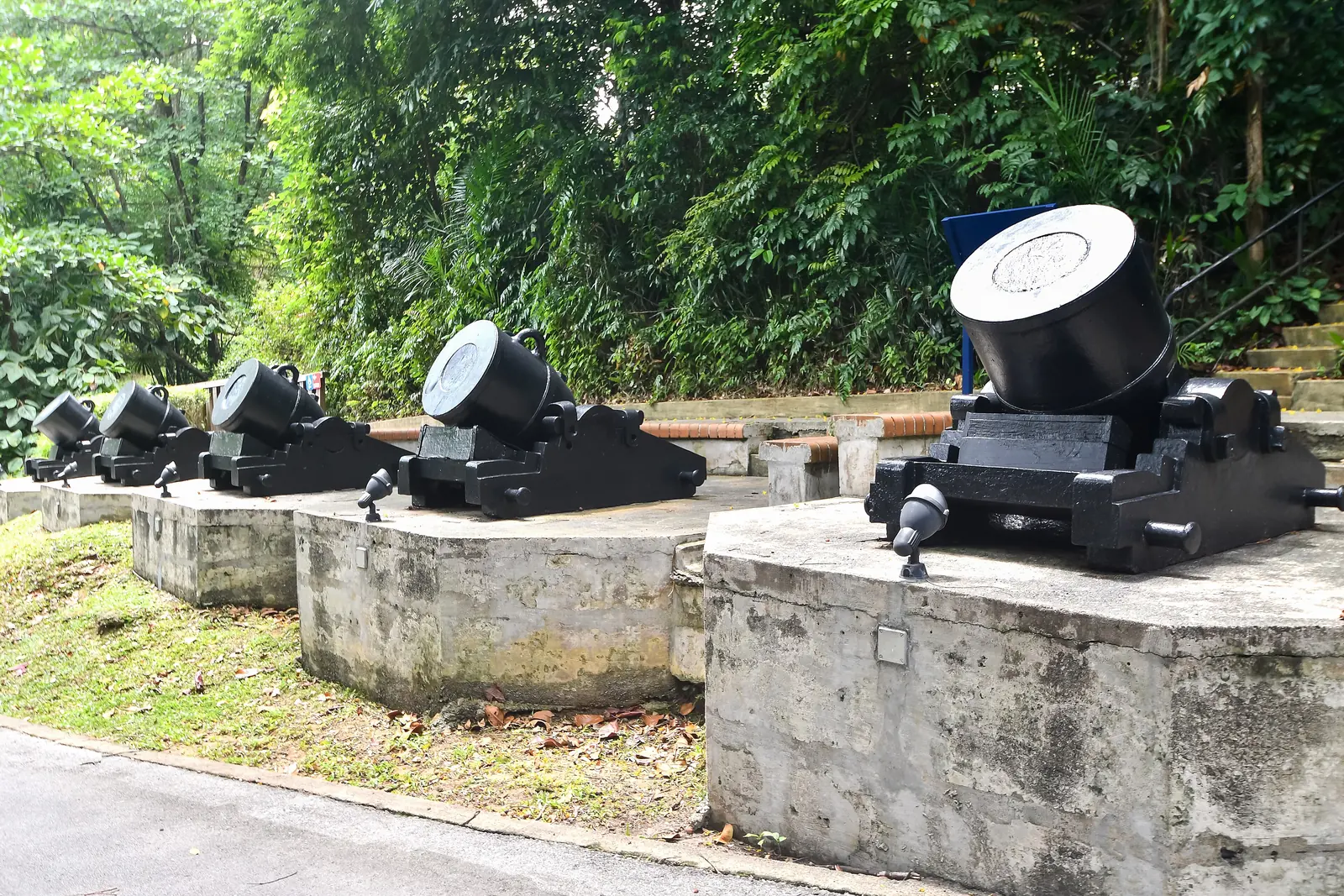 A row of preserved black 13-inch trench mortars on concrete bases among trees at Fort Siloso on Sentosa